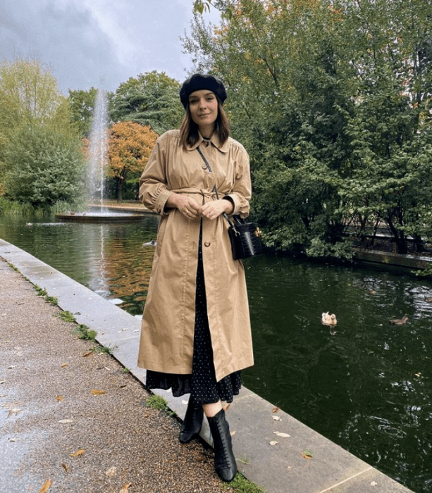 chica de cabello claro usando una boina negra, abrigo largo beige, vestido largo negro con lunares blancos, botines de tacón negros de cuero, bolso mini de mano negro