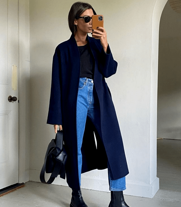 chica de cabello castaño usando lentes de sol, camiseta negra, jeans a la cintura, botas de suela gruesa, saco largo azul marino