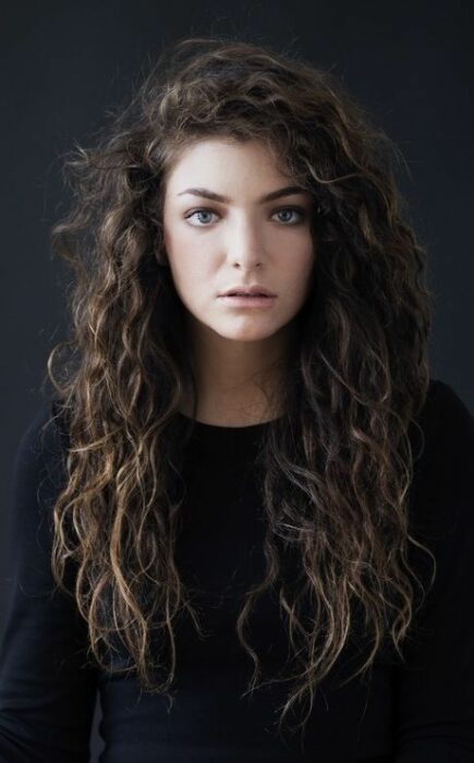 Lorde posando para una foto, llevando suéter negro con cabello largo rizado