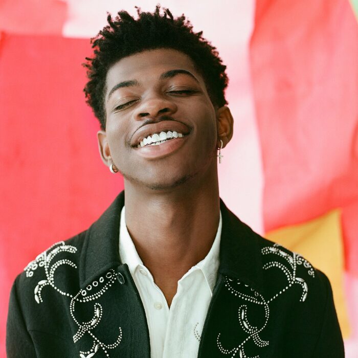 Lil Nas X sonriendo, llevando un caso negro con decoración de lentejuelas