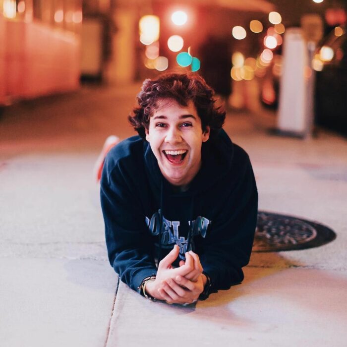 David Dobrik sonriendo, recostado en el piso para una fotografía de noche