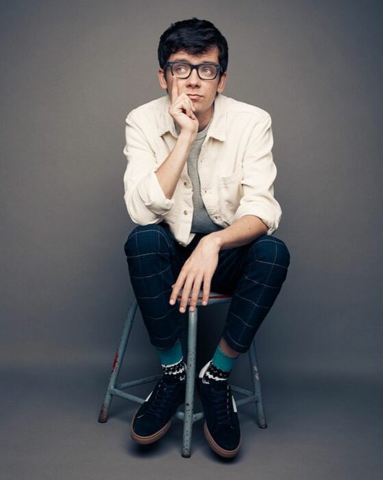 Asa Butterfield sentadop en un banco de madera, posando para una fotografía