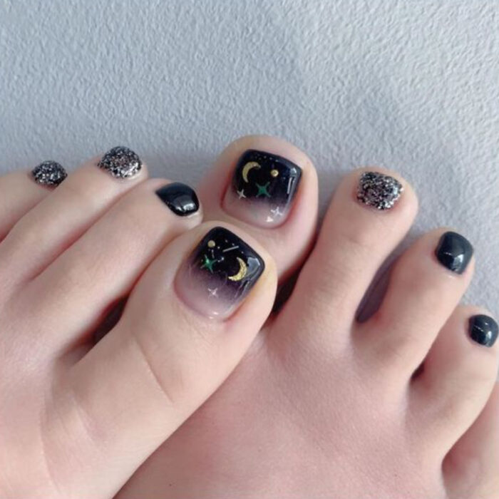 Pedicura en colores negro y nude con detalles de estrellas y lunas doradas