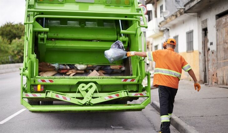 Recolector de basura colocando una bolsa de desechos en el camión de basura