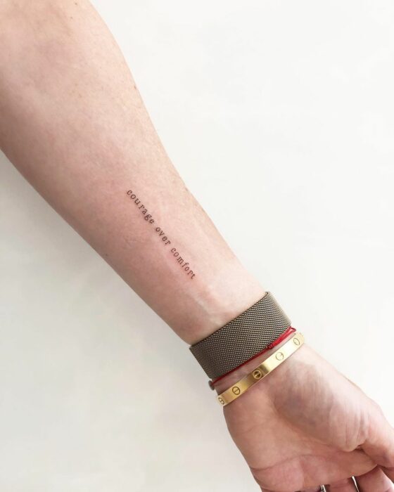 Tatuaje de "courage over comfort" en el brazo 