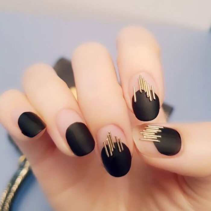 Manicura con diseño de color negro y líneas doradas 