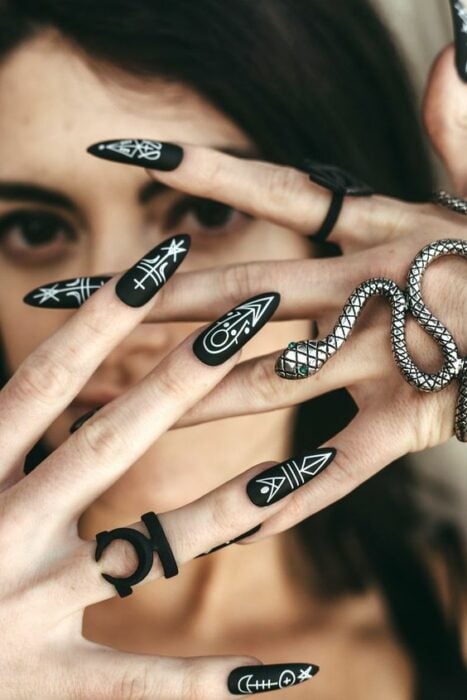 chica con manicura en color negro con estampado blanco de serpientes y simbolos;  Uñas para chicas que aman el ocultismo