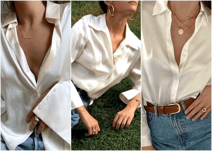 chica con camisa blanca de vestir de seda con joyería dorada, collares chunky, aretes de aro largos, anillos de oro estilo signet y jeans azules