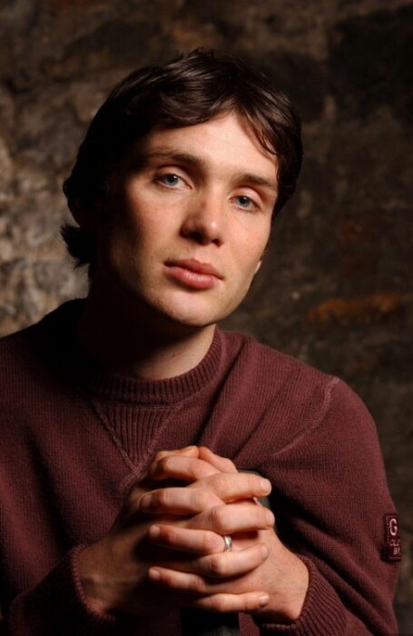 Cillian Murphy con suéter rojo y de manos cruzadas