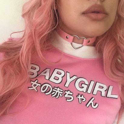 Chica de cabello rosa, vistiendo blusa rosa y una gargantilla de corazón 