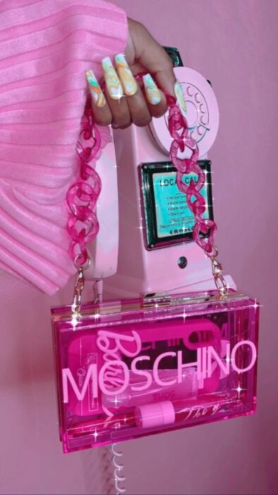Mano sosteniendo bolso rosa rectangular transparente con cadena de plástico