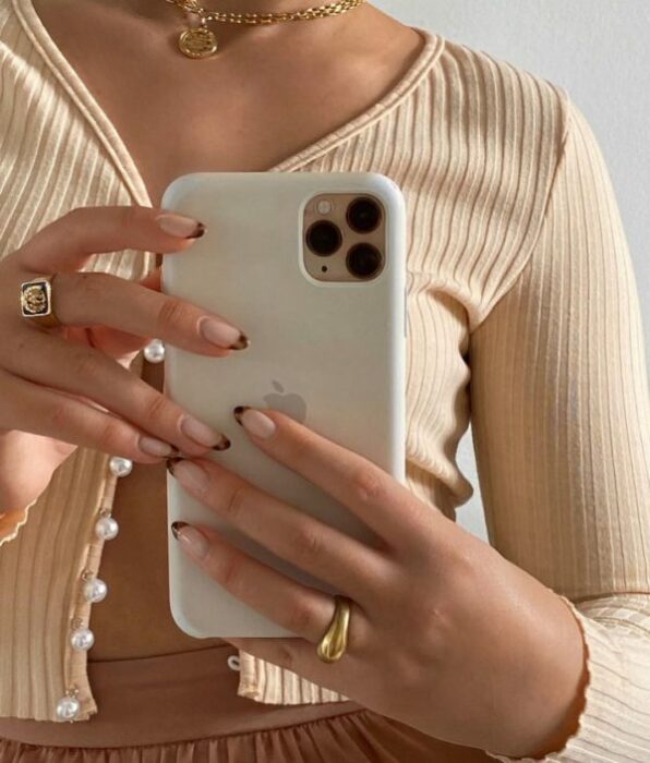 Chica tomándose selfie con iPhone sujetándolo con uñas con punta de animal print 