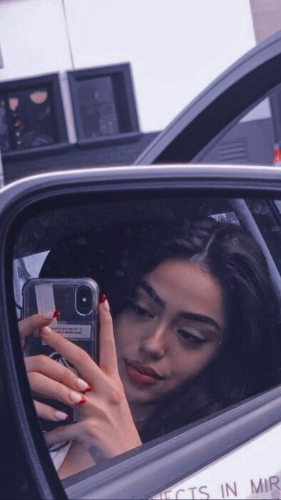 Chica morena clara tomándose selfie en espejo lateral de automóvil 