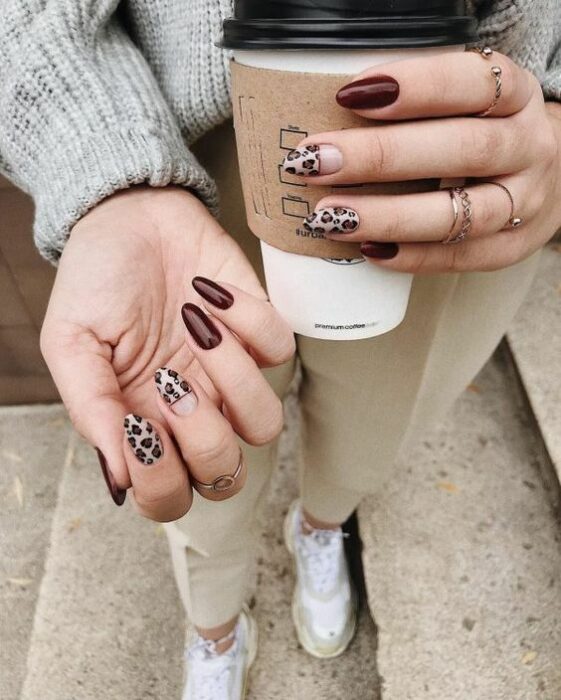 Chica sosteniendo un vaso de café y mostrando sus uñas color vino y beige con detalles de leopardo 