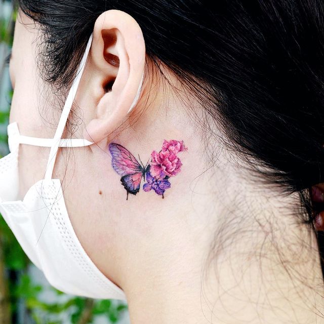 Tatuaje de mariposa detrás del oido en tonos rosas con flores desprendidas;  15 Bellos tatuajes con mariposas para iniciar una metamorfosis