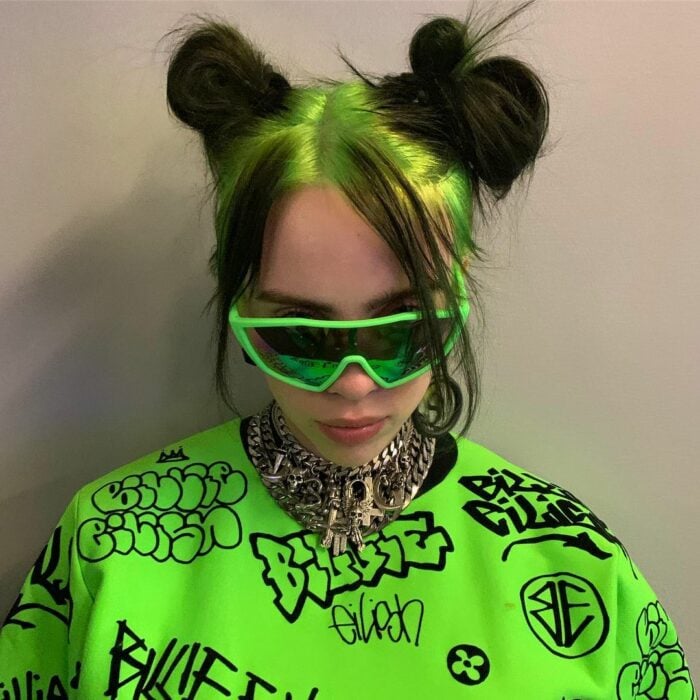 Billie Eilish usando dos chonguitos mientras tiene un cabello teñido de verde con negro 