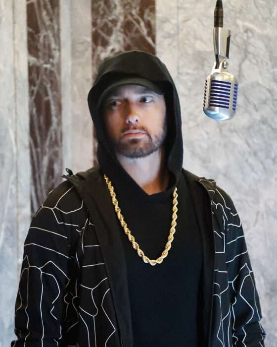 Eminem usando una playera negra, sudadera con detalles grises y una cadena dorada