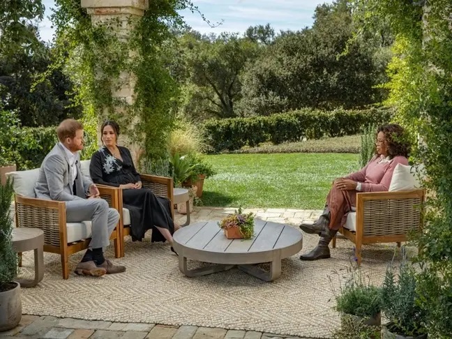 Harry y Meghan sentados en un sofá mientras están siendo entrevistados por Oprah en el jardín de su casa 