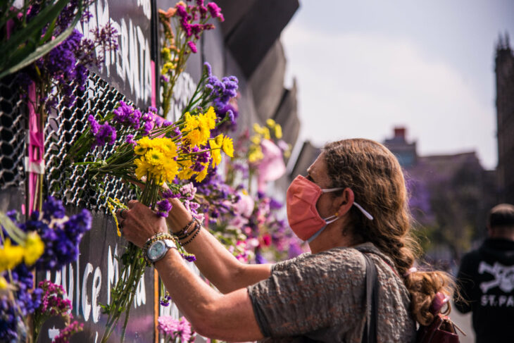 Mujer colocando flores sobre una vaya colocada para frenar las marchas del 8 de marzo 2021 