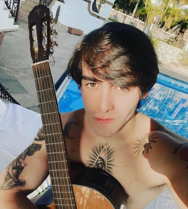Julián Figueroa sentado frente a una picina tomando el sol y sujetando su guitarra 