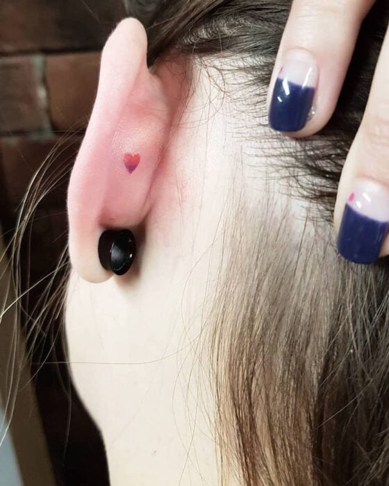 Chica con un tatuaje en la oreja en forma corazón en color rojo