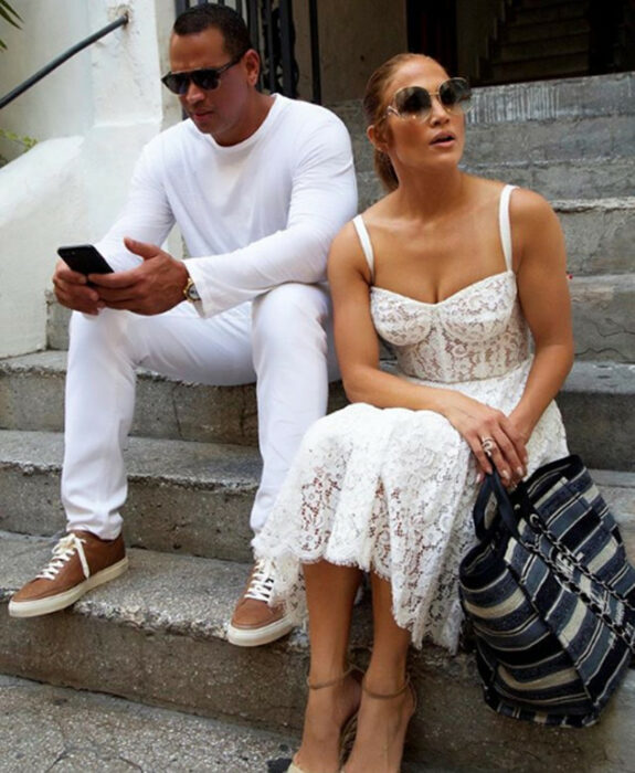 Jennifer Lopez y Alex rodriguez sentados en unas escaleras mirando sus teléfonos 