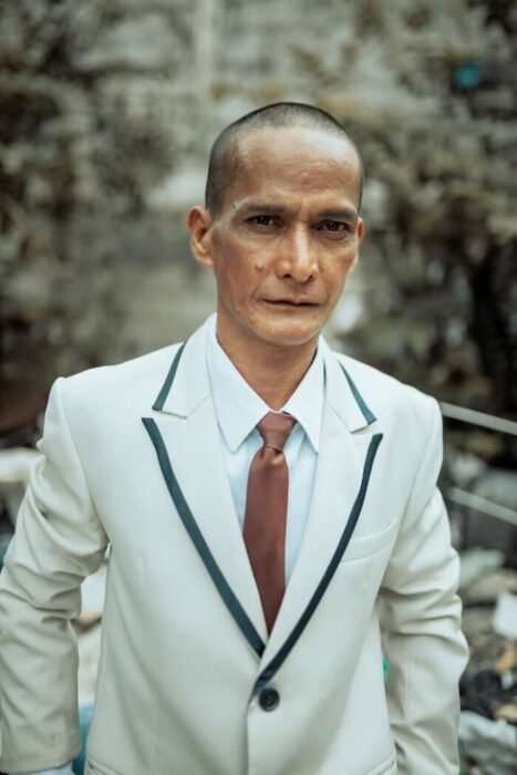 Hombre posando para una foto el día de su boda mientras usa un traje de color blanco 