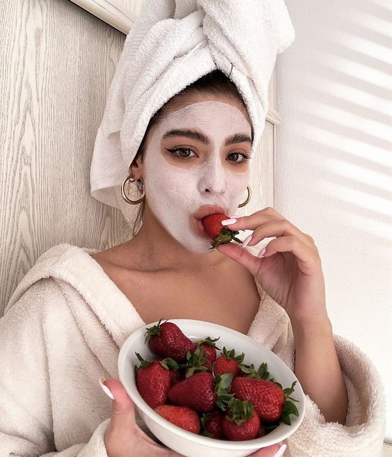 Chica llevando una mascarilla mientras come fresas; Mascarillas con huevo para una piel bonita