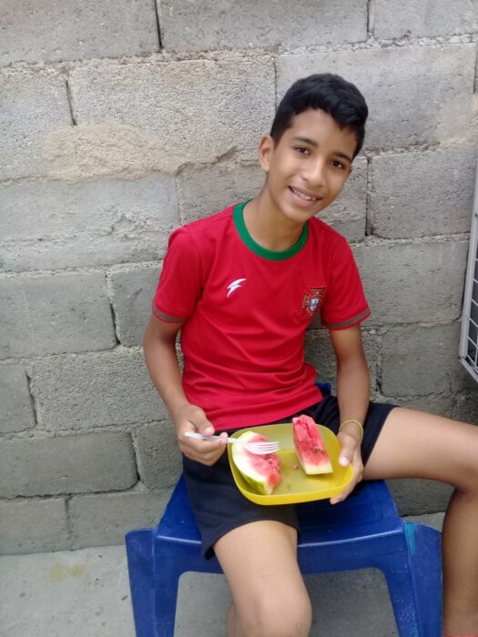 Niño Samuel Mendoza sentado comiendo fruta mientras posa para una fotografía 