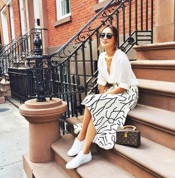 Chica usando camisa color blanco, falda del mismo color con detalles en color negro y tenis blancos