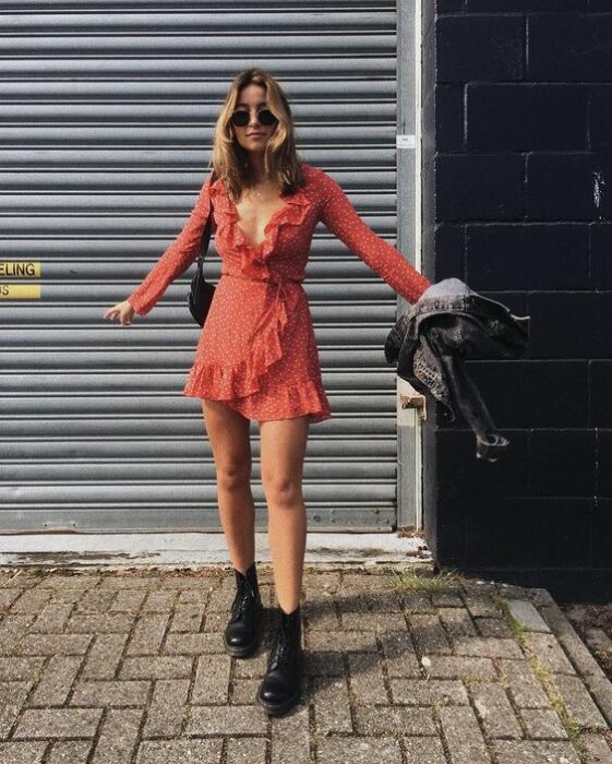 Chica usando un vestido color rojo quemado con escote V, de manga larga, usando botines negros