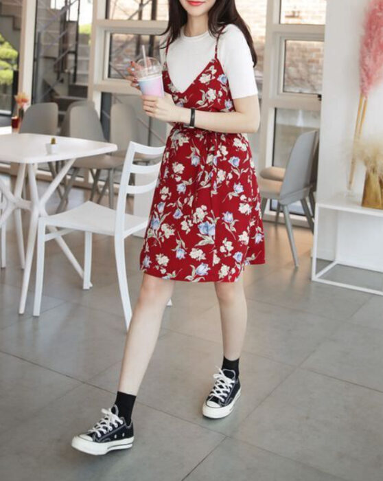 Chica usando un vestido color rojo con estampado de flores en colores claros, con una blusa blanca debajo y converse negros