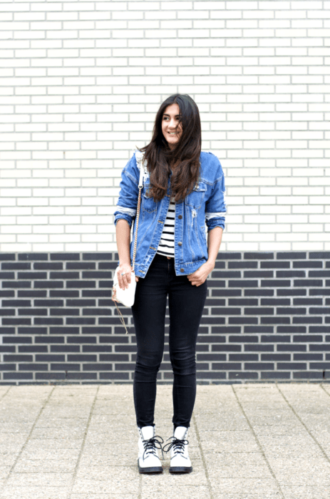 Chica usando un look casual con jeans negros, chaqueta de mezclilla y blusa a rayas acompañada de unas botas Dr. Martens 