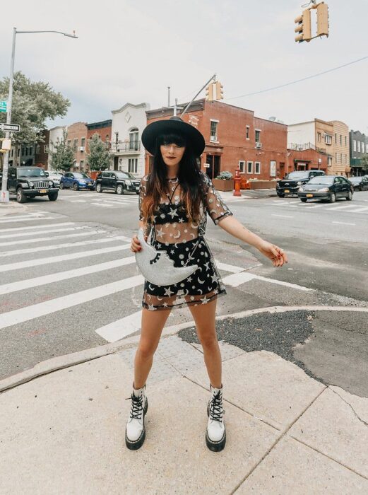 Chica posando para una fotografía mientras está usando un vestido de estrellas color plateado y botas Dr. Marten color blancas con cintas negras 