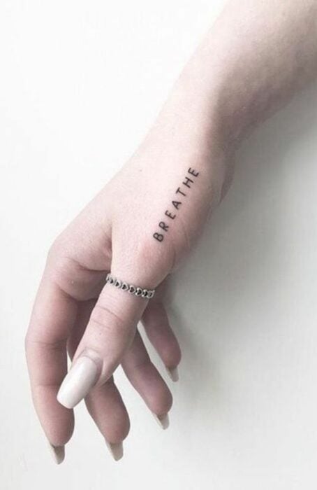 Chica con un tatuaje en la mano con la frase Breathe 