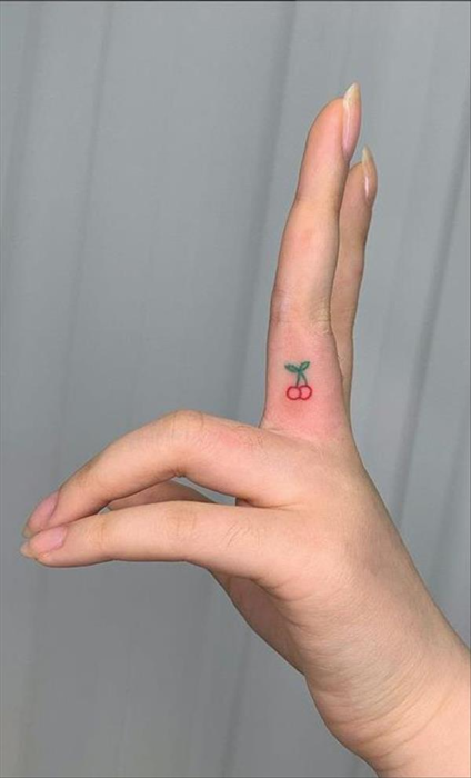 Chica con un tatuaje en forma de cerezas en el dedo medio 