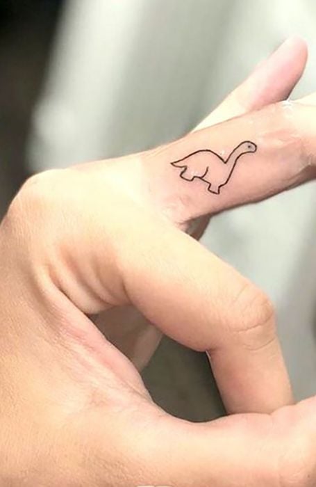 Chica con un tatuaje en forma de dinosaurio en el dedo medio