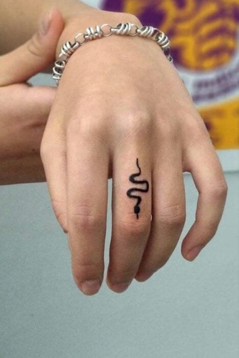Chica con un tatuaje en forma de serpiente en el dedo medio 