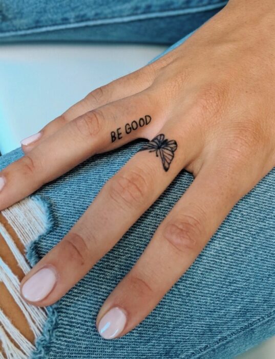 Chica con un tatuaje en forma de mariposa y con letras en el dedo medio y anular 