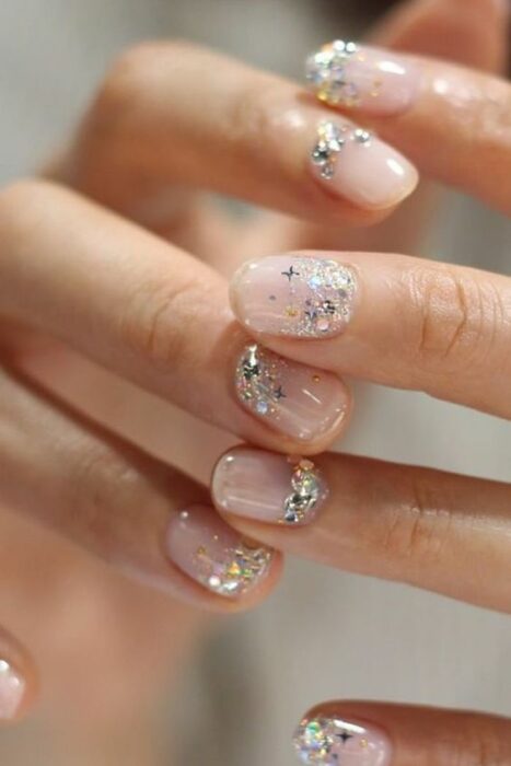 Manicura con fondo color nude y detalles de glitter color plateado