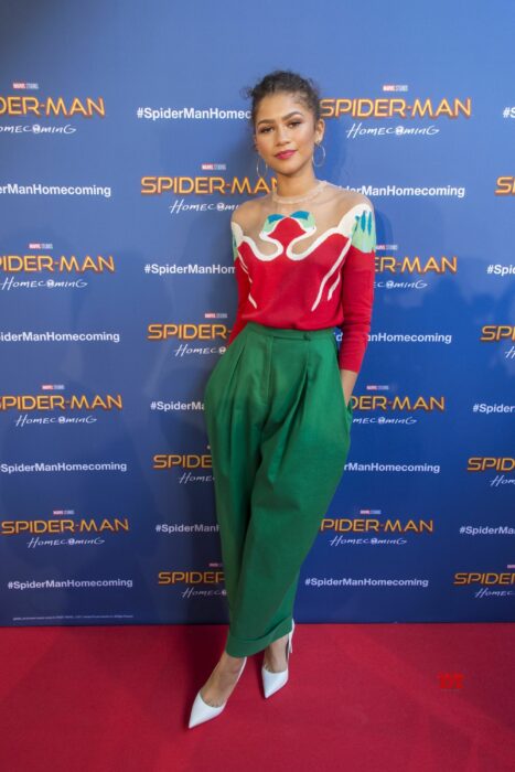 Zendaya usando un conjunto de color verde con una blusa de color roja y detalles en color azul 