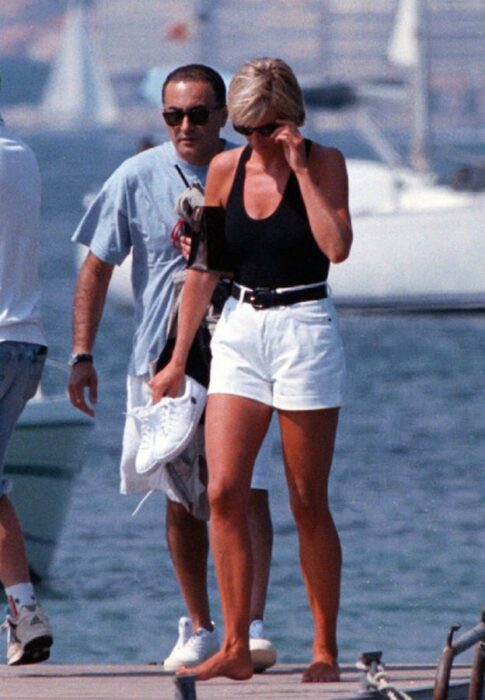 Diana Spencer usando unos shorts de color blanco con una blusa top de color negro mientras camina por un puerto 