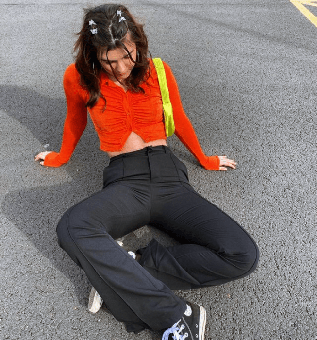 chica de cabello castaño usando cárdigan corto naranja de manga larga, pantalones negros acampanados y tenis converse negros