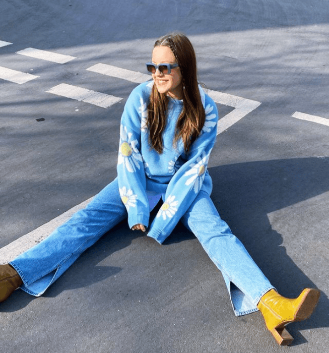 chica de cabello castaño con lentes de sol, suéter celeste con nubes blancas, jeans ajustados y botines amarillos