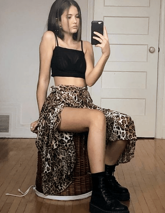 chica de cabello corto usando un crop top negro de tirantes, falda larga abierta de animal print y botines negros de cuero