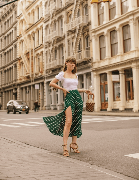 chica de cabello castaño usando una blusa blanca de manga corta, falda larga verde abierta con lunares blancos y sandalias de tacón café claro