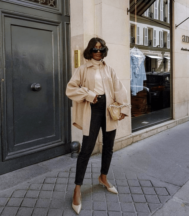 chica morena con cabello oscuro corto usando lentes de sol, jeans negros ajustados, flats beige, top beige y abrigo beige