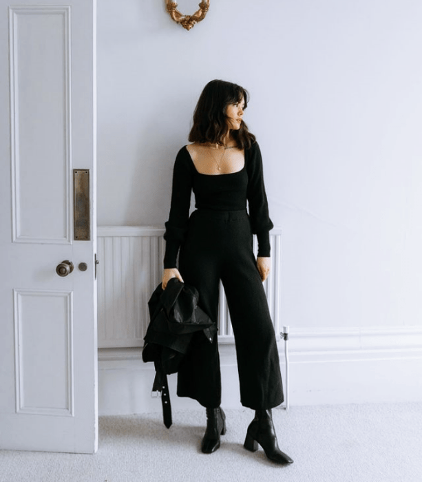 chica de cabello corto con blusa negra de escote cuadrado, jeans negros acampanados, botines negros de tacón y chamarra negra