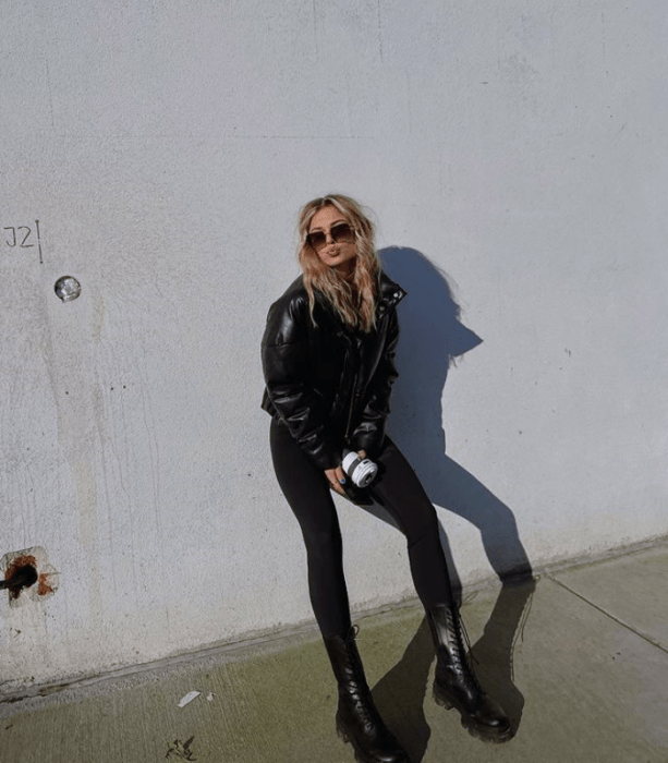 chica rubia con lentes de sol, chamarra de cuero negra, jeans negros ajustados, botines negros de plataforma