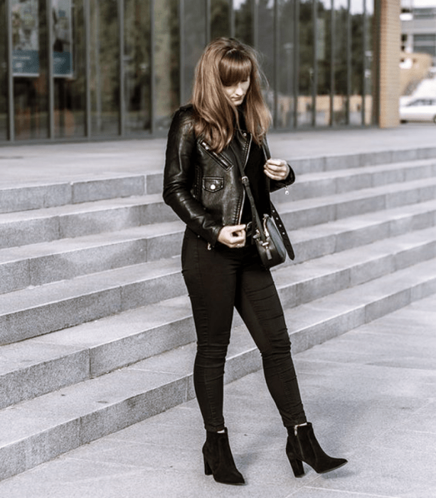 chica de cabello largo oscuro usando un top negro, chamarra de cuero, jeans ajustados negros, botines de tacón negros